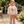 A young child stands on a stone path in a garden wearing a light pink sweatshirt with a deer graphic and matching patterned pants, holding a plush toy.