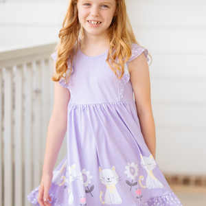 Young girl wearing a purple dress with cat and flower patterns indoors.