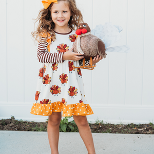 A young girl wearing a cream ground turkey themed printed dress and holding a turkey stuffed animal, lifestyle, Millie Loves Lily