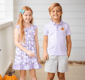 A girl wearing a lilac halloween themed printed dress and a boy wearing a lilac and white striped polo with a pumpkin on the left chest and khaki shorts standing on a porch, lifestyle- Millieloveslily.com