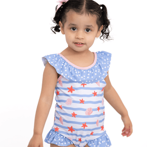 A young girl wearing a blue stripe 1-pc swimsuit with seashells and starfish and blue dot ruffles, lifestyle