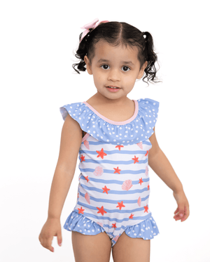 A young girl wearing a blue stripe 1-pc swimsuit with seashells and starfish and blue dot ruffles, lifestyle