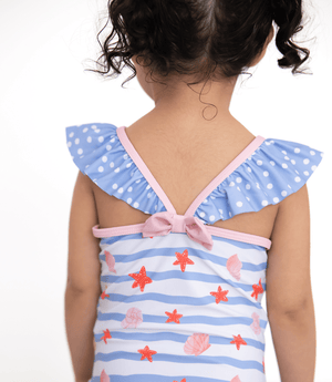A young girl wearing a blue stripe 1-pc swimsuit with seashells and starfish and blue dot ruffles and a pink back bow, backview, lifestyle