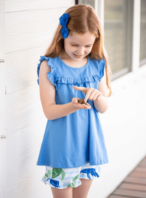 Girl standing on a porch holding a turtle wearing a blue  Top and Turtle Print Ruffle short, lifestyle
