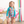 A young  girl wearing a long sleeve turquoise floral and dot rashguard set  holding a straw purse standing in a pool room, lifestyle- Millieloveslily.com