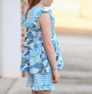 A young girl standing outside wearing a mint turtle ptinted top and matching stripe shorts, lifestyle