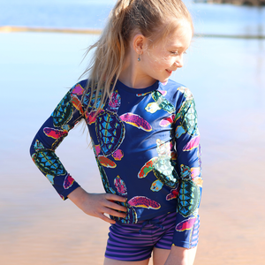 A young girl wearing a Navy Turtle patterned Rashguard and stripe swim shorts lifestyle