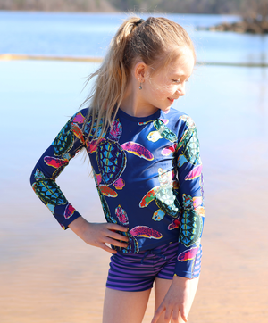 A young girl wearing a Navy Turtle patterned Rashguard and stripe swim shorts lifestyle