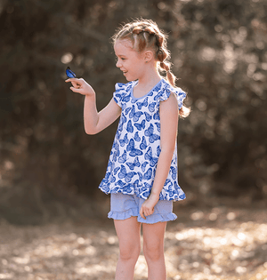 Young girl wearing a  Periwinkle Butterfly Printed Top and Solid Short holding a butterfly, lifestyle