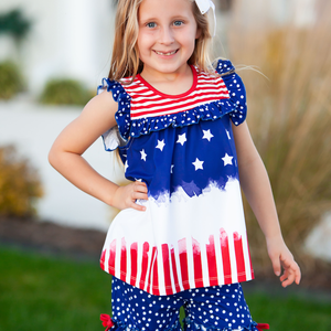 A young girl standing outside wearing a matching red, white & blue stars and stripe short set with her hand on her hip, lifestyle