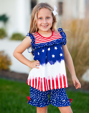 A young girl standing outside wearing a matching red, white & blue stars and stripe short set with her hand on her hip, lifestyle