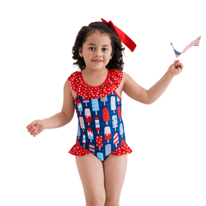 A young girl wearing a red,white & blue popsicle print swimsuit standing in front of a white background, lifestyle