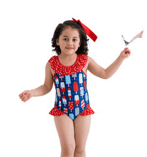 A young girl wearing a red,white & blue popsicle print swimsuit standing in front of a white background, lifestyle