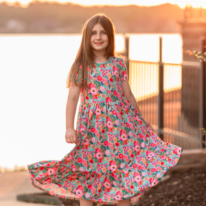 A young girl wearing a turquoise floral hi-low mid-length dress with short sleeves standing in front of a lake, lifestyle