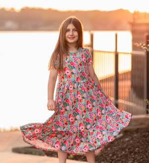 A young girl wearing a turquoise floral hi-low mid-length dress with short sleeves standing in front of a lake, lifestyle