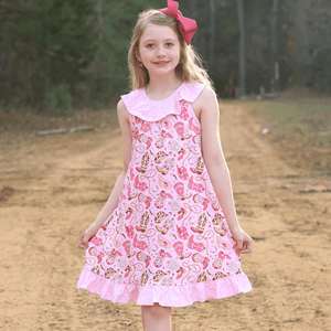 A young girl standing on a dirt path wearing a Pink rodeo themed Dress with a pink bow in her hair, lifestyle 