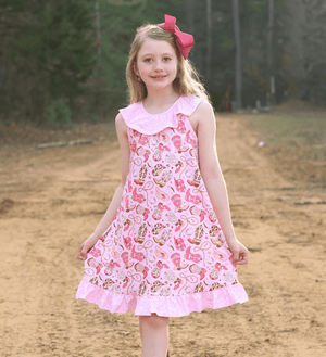 A young girl standing on a dirt path wearing a Pink rodeo themed Dress with a pink bow in her hair, lifestyle 