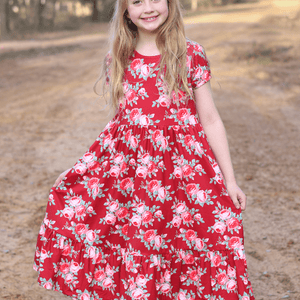 A young girl wearing a red floral hi-low mid-length dress standing outside is a forest like area, lifestyle