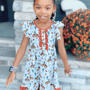 A young girl standing outside wearing a  Rodeo themed  Ruffle Front Angel - Sleeve Dress - Millieloveslily.com