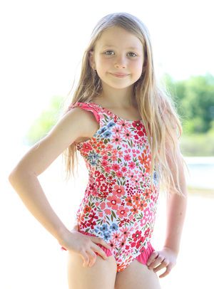 a young girl wearing a Coral Floral Ruffle - Accent One - Piece swimsuit standing outside, lifestyle, front- Millieloveslily.com