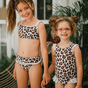 Two young girls wearing leopard skin swimsuits holding hands standing outside, lifestyle, front- Millieloveslily.com