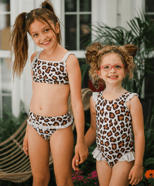 Two young girls wearing leopard skin swimsuits holding hands standing outside, lifestyle, front- Millieloveslily.com