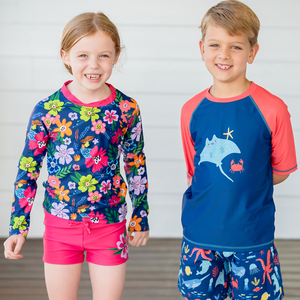 A young girl and boy wearng rashguard sets standing in front of a white wall, lifestyle