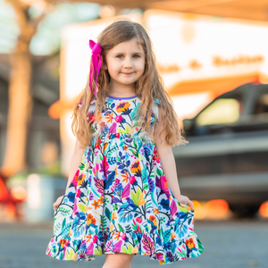 A young girl standing outside wearing a multicolor floral angel wing dress, lifestyle
