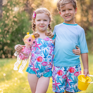 A young boy and young girl wearing matching ocean themed swimsuits holding toys standing in the grass, lifestyle, front Millieloveslily.com