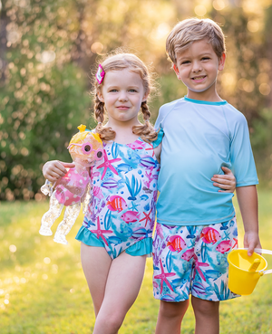 A young boy and young girl wearing matching ocean themed swimsuits holding toys standing in the grass, lifestyle, front Millieloveslily.com
