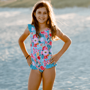 Young girl wearing a  Turquoise  Floral Ruffle Accent One Piece swimsuit standing on the beach, lifestyle, front Millieloveslily.com