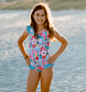 Young girl wearing a  Turquoise  Floral Ruffle Accent One Piece swimsuit standing on the beach, lifestyle, front Millieloveslily.com