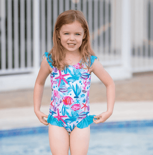 young girl wearing an ocean themed One - Piece swimsuit standing in a pool, lifestyle, front- Millieloveslily.com