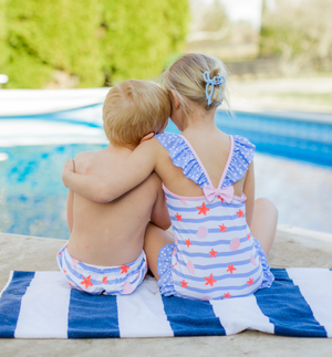 A boy and girl sitting poolside on a stripe towel, back