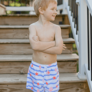 Boy wearing blue stripe swim trunks in front of steps outside, front
