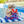 Boys and girl sitting poolside on a stripe towel wearing red, white and blue swimsuits, back
