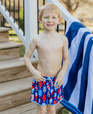 Boy wearing Red, Wht, & Blue Popsicle print Swim Shorts standing in front of a pool, front