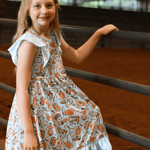 Young girl wearing a blue rodeo themed   Dress standing at a metal fence, lifestyle, front - Millieloveslily.com