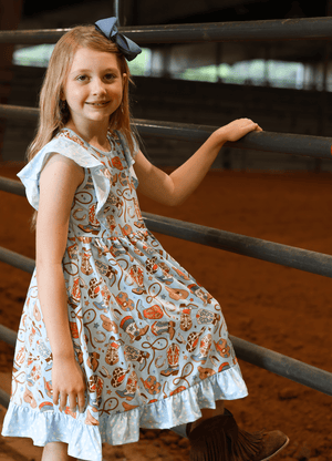 Young girl wearing a blue rodeo themed   Dress standing at a metal fence, lifestyle, front - Millieloveslily.com