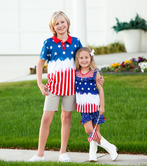 A young girl and young boy standing outside wearing matching red, white & blue stars and stripe outfits with their arms around each other, lifestyle